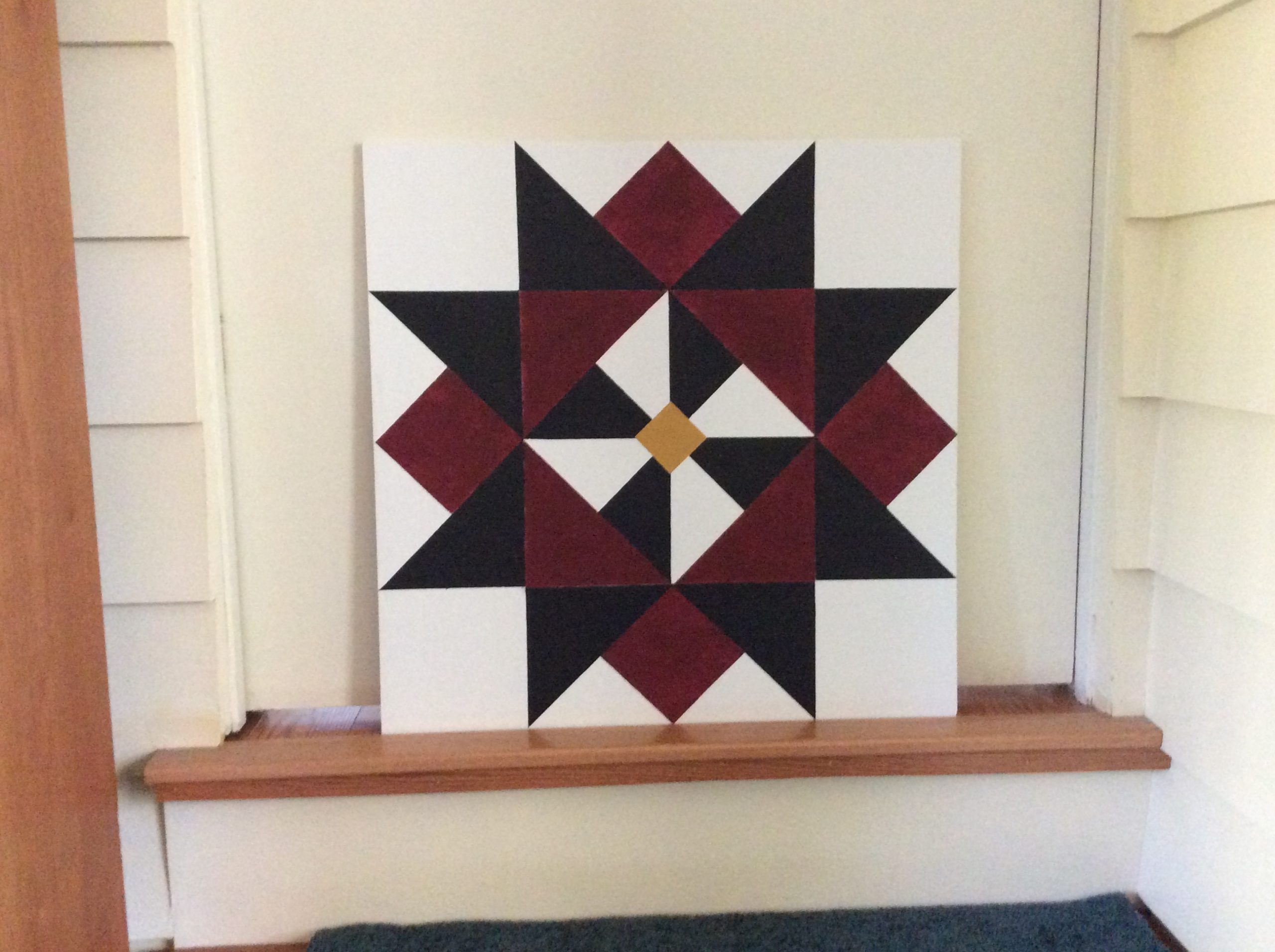 A geometric design on a barn quilt square made up of red, black and yellow triangles.