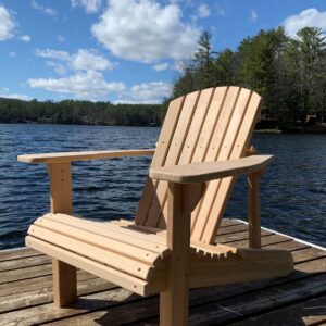A wooden Adirondack Chair sits on a dock with a blue sky in the background