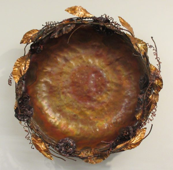 A copper bowl with copper vines decorating the rim.