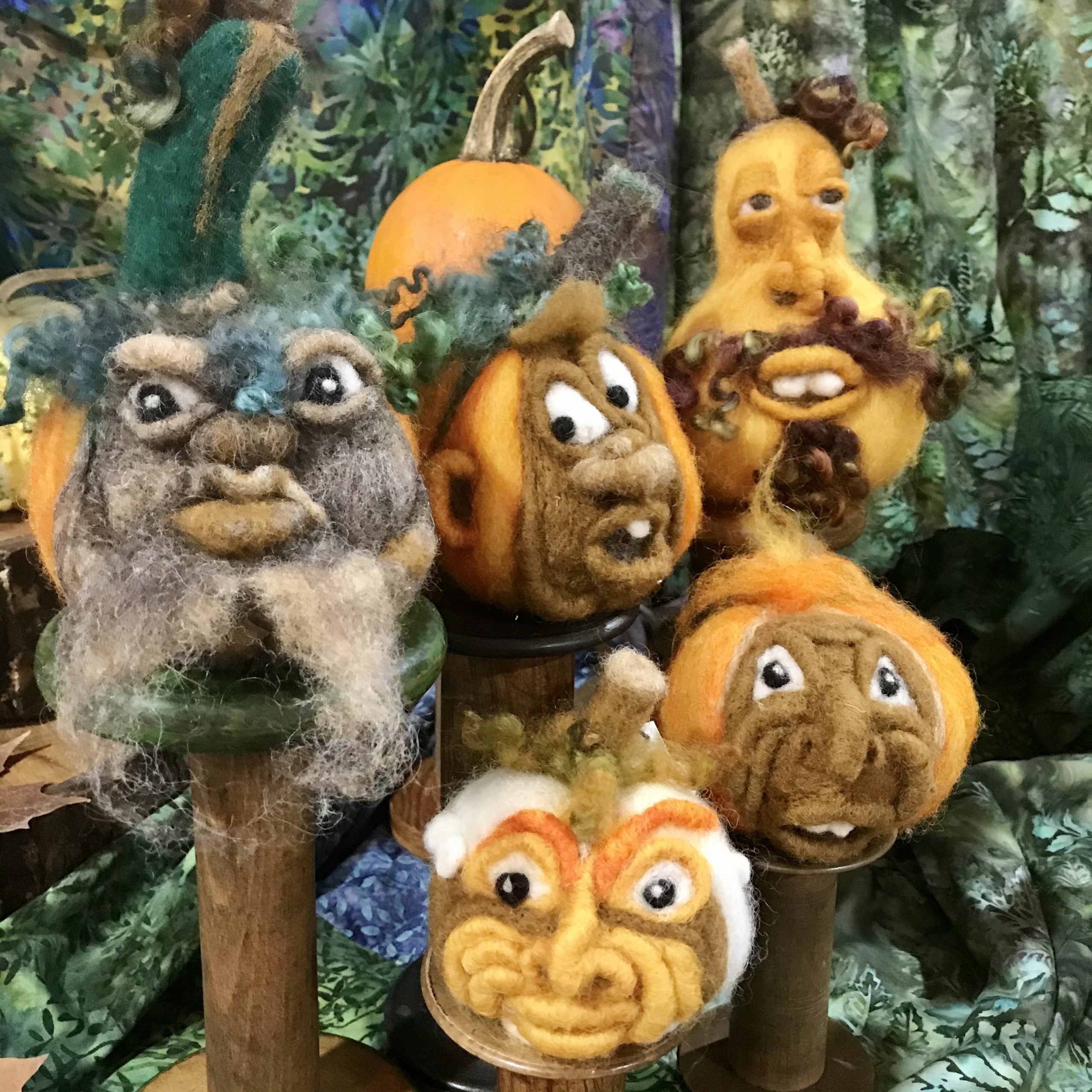 A grouping of 5 needle felted fall gourds with faces in various expressions.