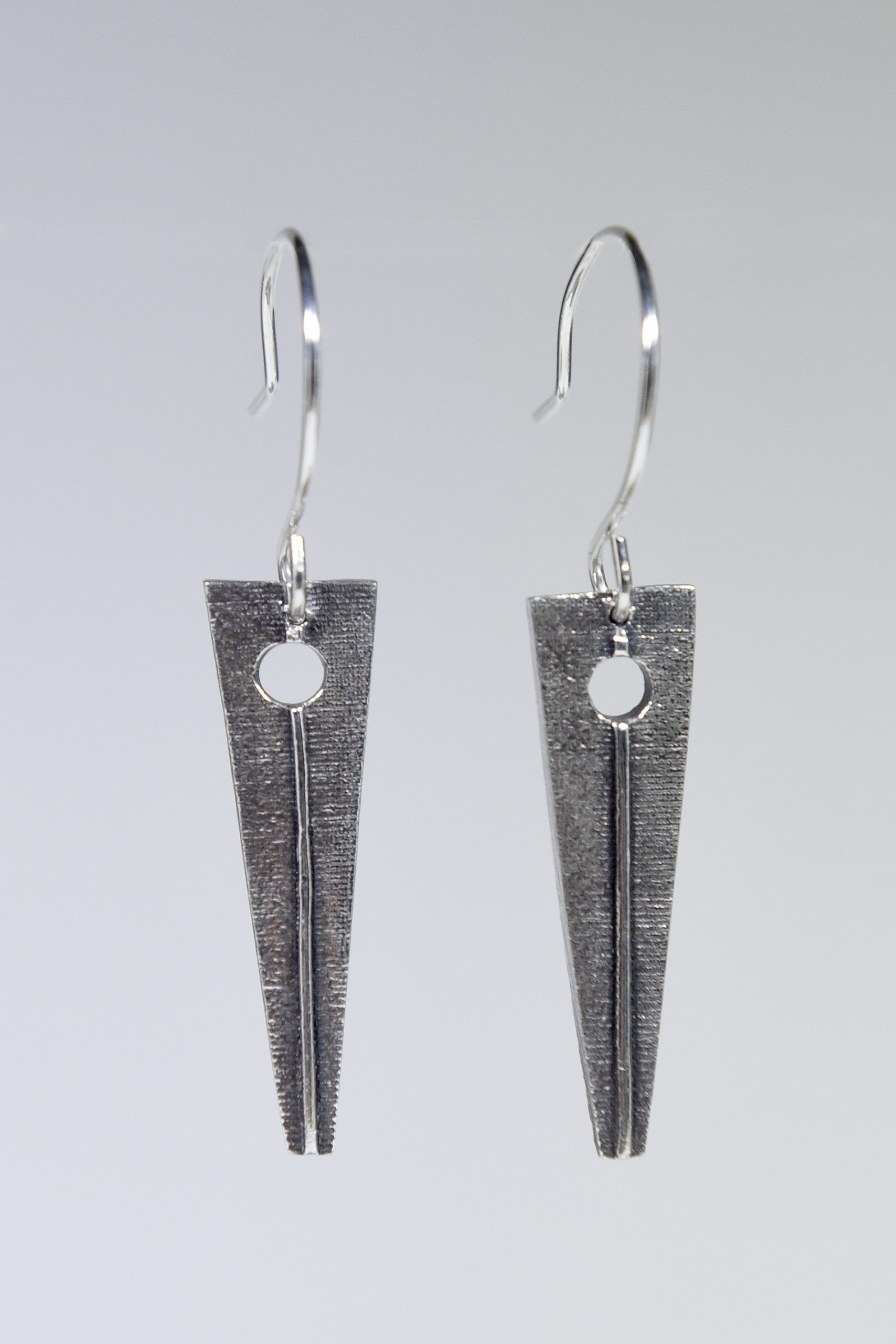 A pair of silver triangular dangling earrings on a grey background.