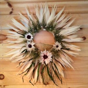 A wreath made of corn husks and decorated with flowers hangs on a wall.