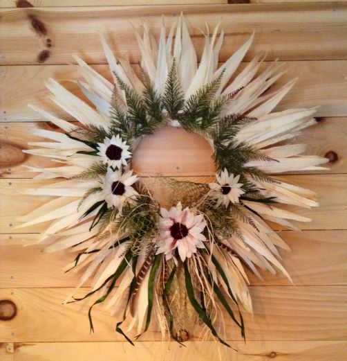 A wreath made of corn husks and decorated with flowers hangs on a wall.