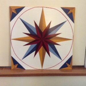 A geometric design on a barn quilt square made up of red, blue and yellow triangles.